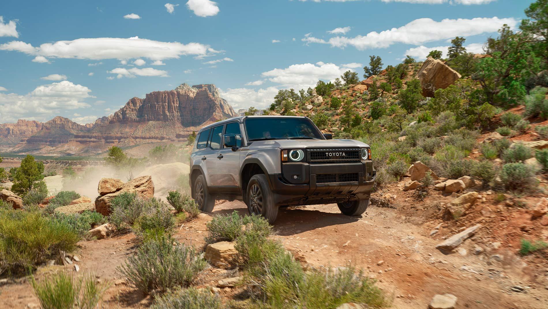 2025 Toyota Land Cruiser Hybrid driving down a dirt road in the rocky mountains