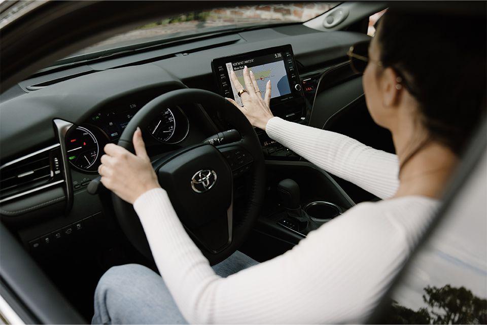 woman sitting in the drivers seat of a Toyota using the navigation map on the large touchscreen