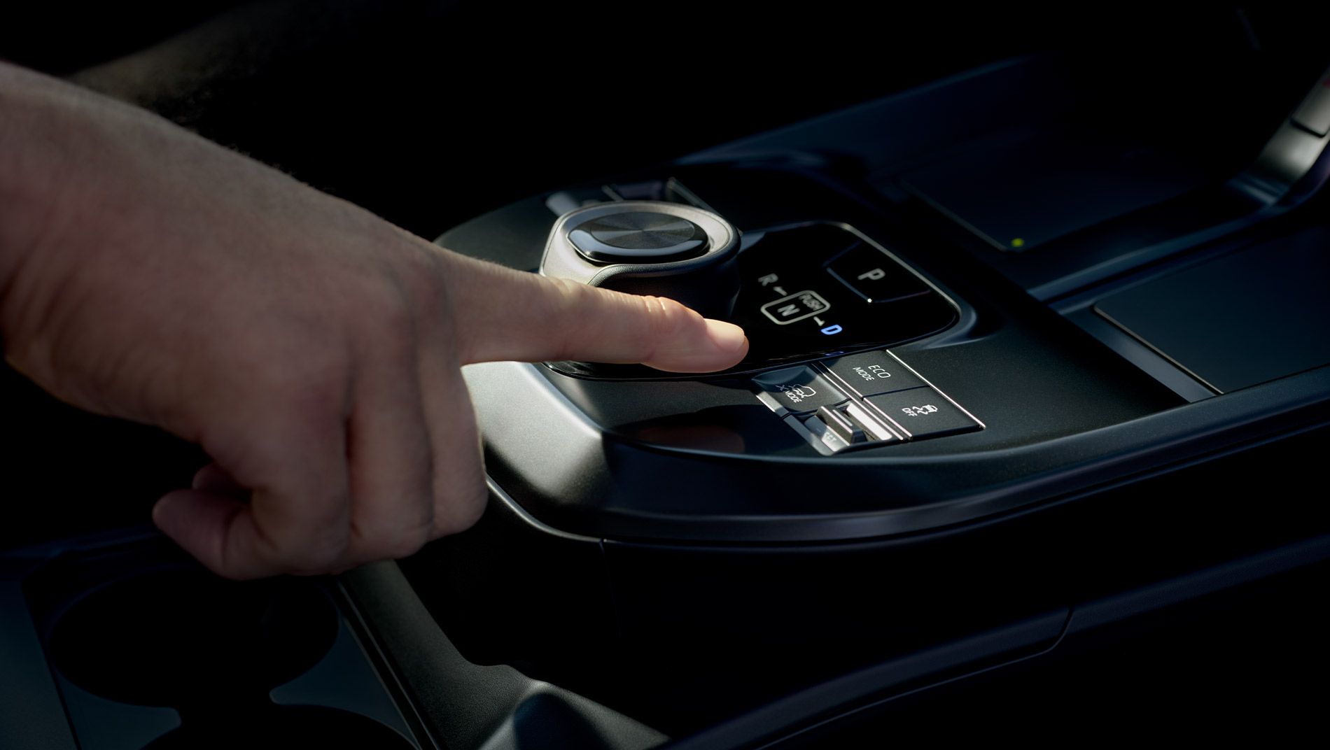 A close-up of a hand pressing a button on a modern car’s center console, featuring electronic gear controls and a digital display.
