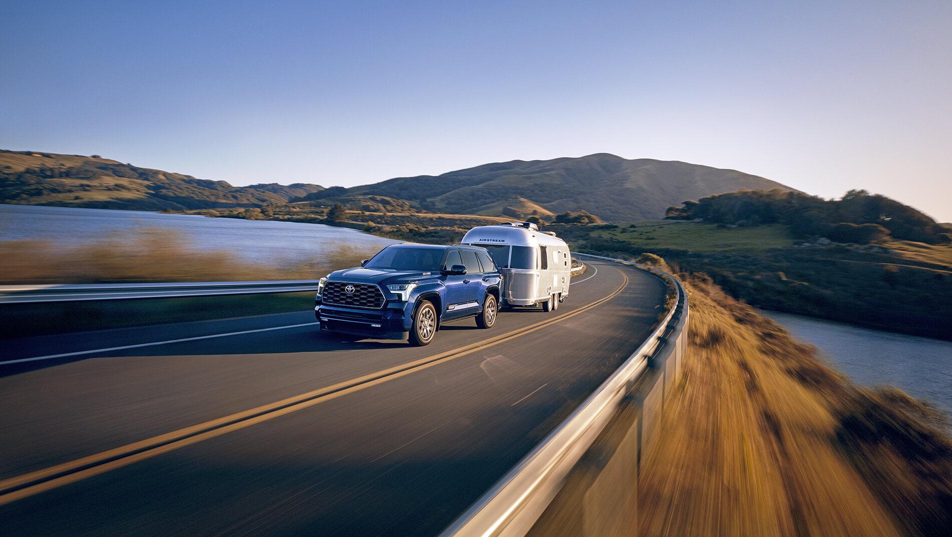 Blue Toyota Sequoia pulling a travel trailer across a mountain lake