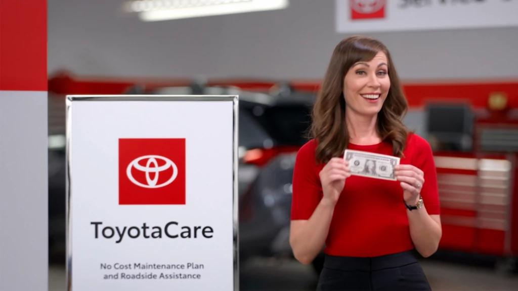 ToyotaCare no cost maintenance plan and roadside assistance sigh with Toyota employee standing next to it holding a dollar bill