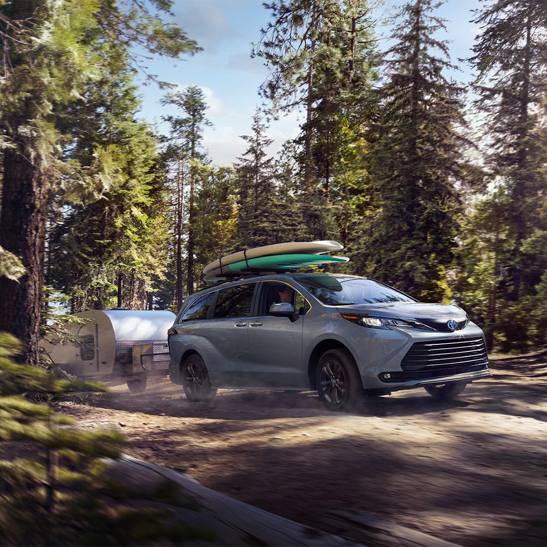 Toyota SUV pulling a camper through the woods with 2 paddle boards on top of the cross bars roof rack