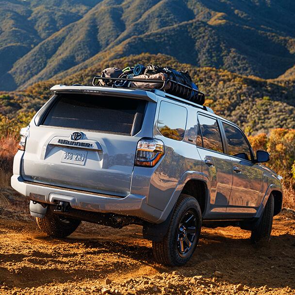 grey Toyota 4Runner with cargo carrier on roof racks driving down a dusty mountain road