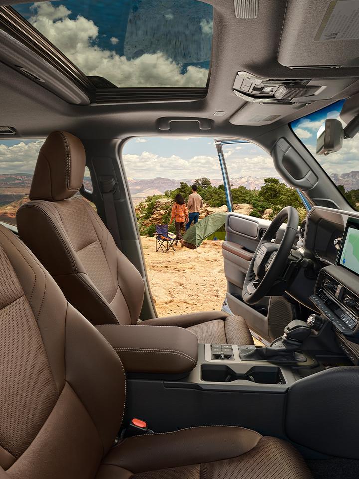2024 Toyota Land Cruiser hybrid showing the interior with sunroof and 2 people outside the open car door with camping chairs ready to set up on the mountain top