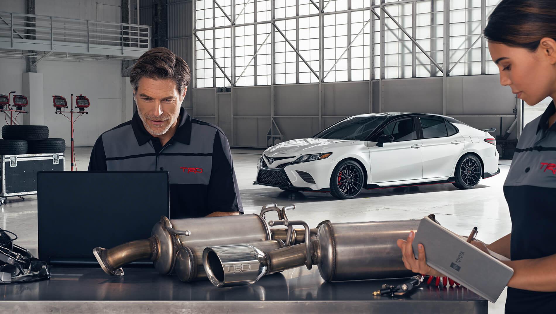 2 Toyota certified technicians work on a white Toyota Camry in a large Toyota Service Center