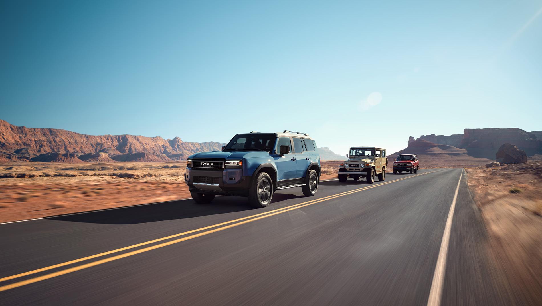 Blue 2025 Toyota Land Cruiser driving down a mountain road followed by older generations of Toyota Land Cruisers