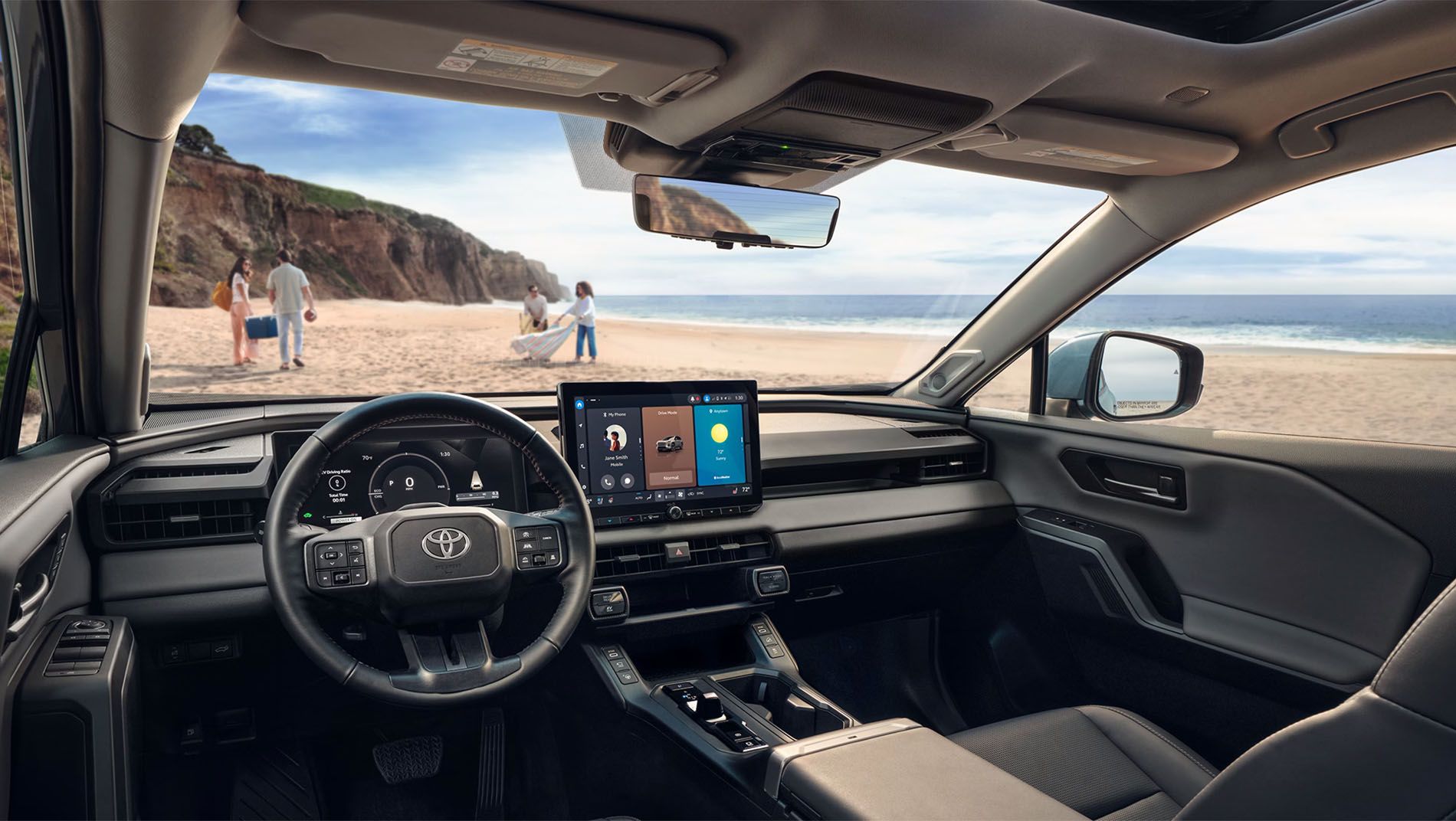 View from inside a modern Toyota vehicle parked at the beach, showing the dashboard, touchscreen display, steering wheel