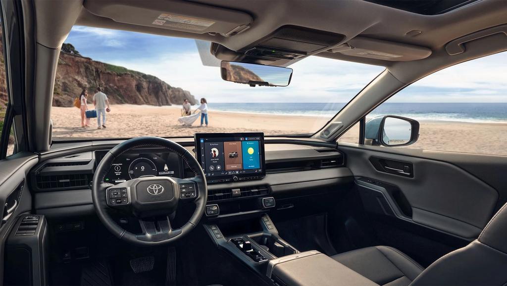 View from inside a modern Toyota vehicle parked at the beach, showing the dashboard, touchscreen display, steering wheel