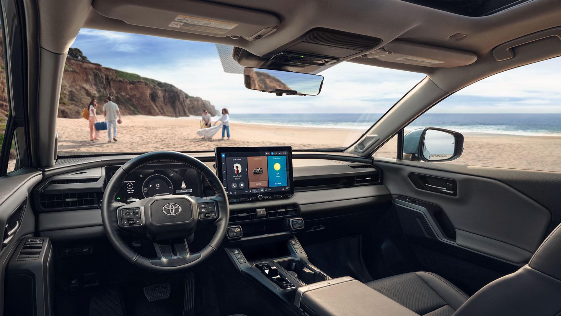 View from inside a modern Toyota vehicle parked at the beach, showing the dashboard, touchscreen display, steering wheel
