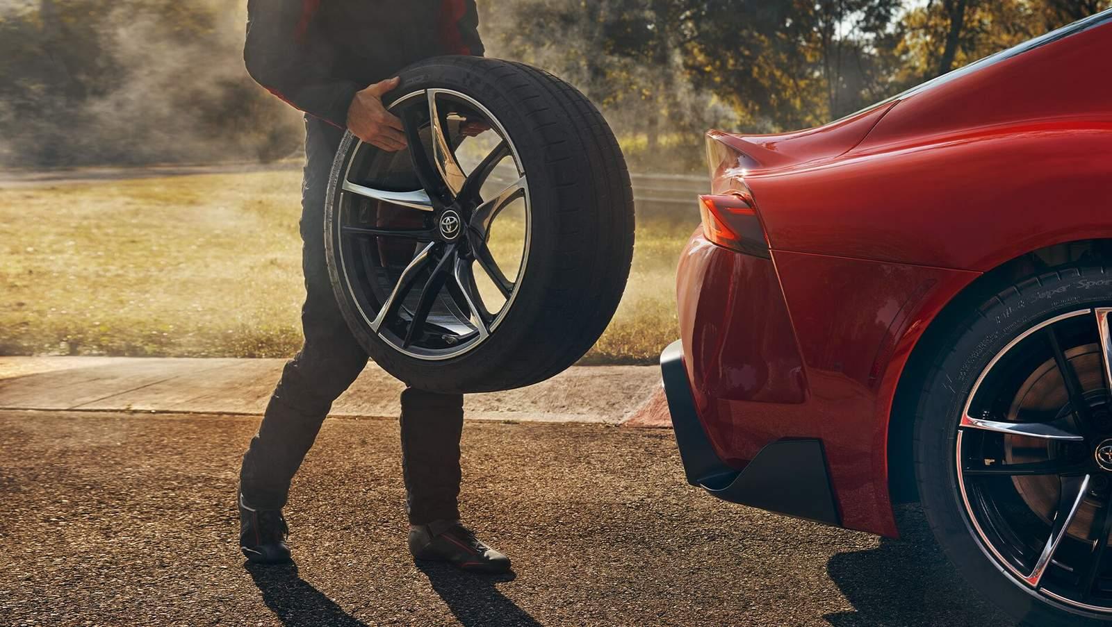 Toyota certified technician bringing a new tire to a red Toyota Supra