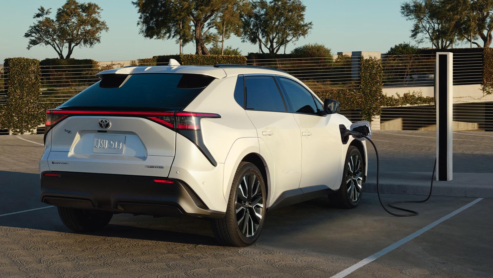 A white electric SUV is parked at a charging station outdoors, with the charging cable plugged into the car.