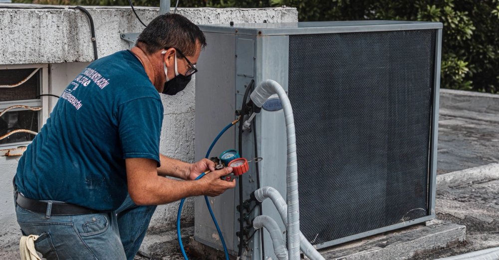 A technician connecting gauges and hoses to an outdoor air conditioning unit