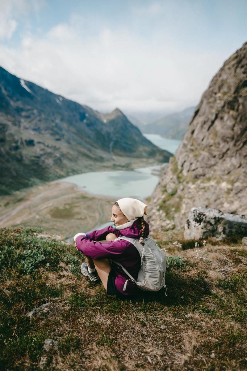 A hiker resting on the ridge above a green lake