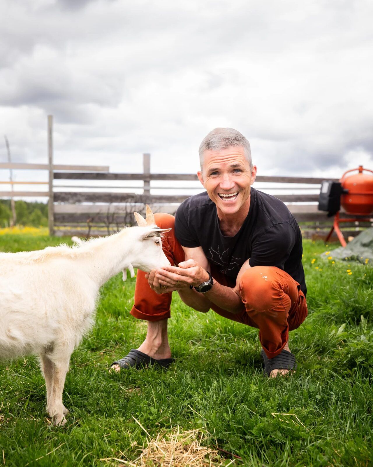 Alexander Medin crouching in the grass with a goat at Nøsen