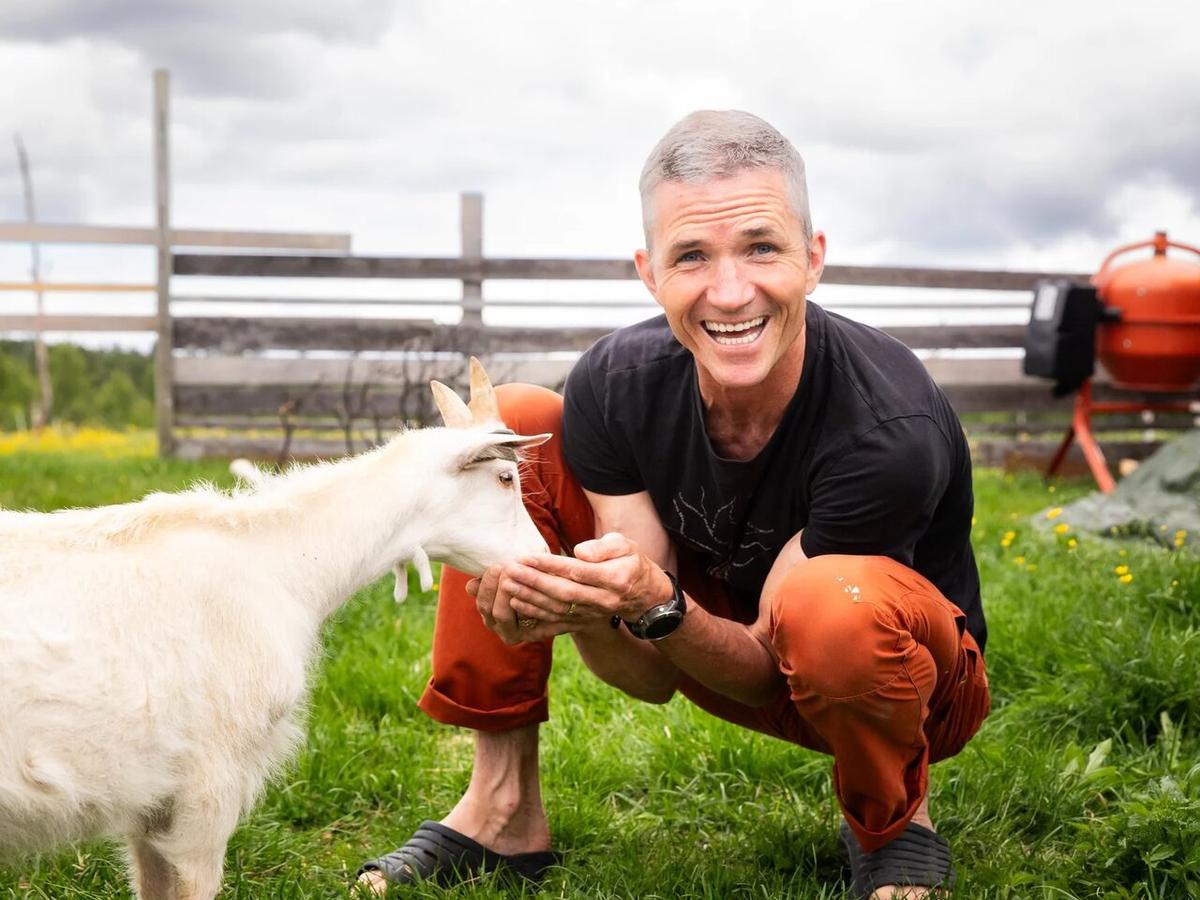 Alexander Medin crouching in the grass with a goat at Nøsen
