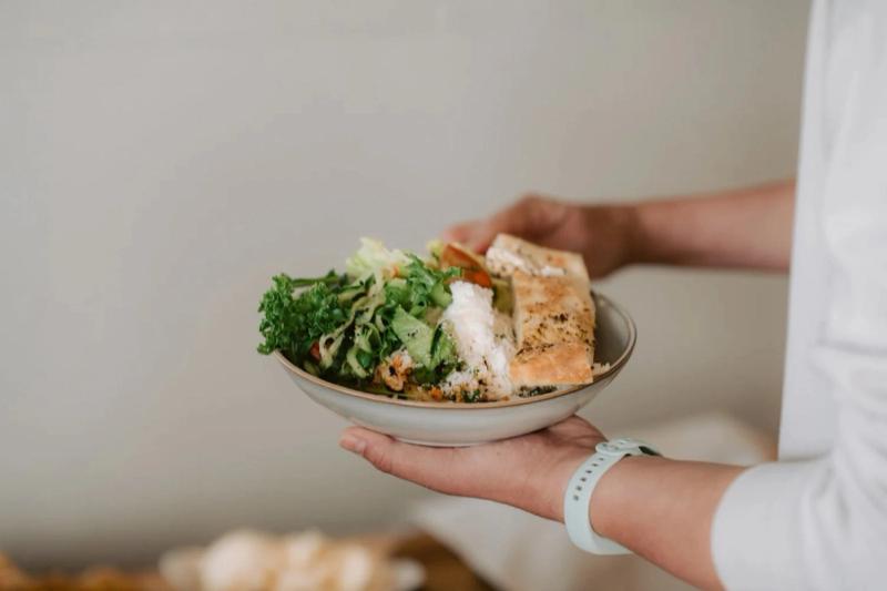 A hand holding a bowl of salad and vegetarian food