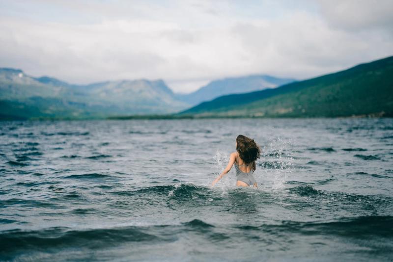 A woman wading into the lake, mountains across the water