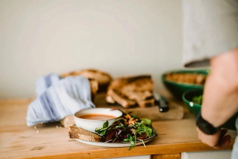 A bowl of soup with bread and salad on a wooden counter