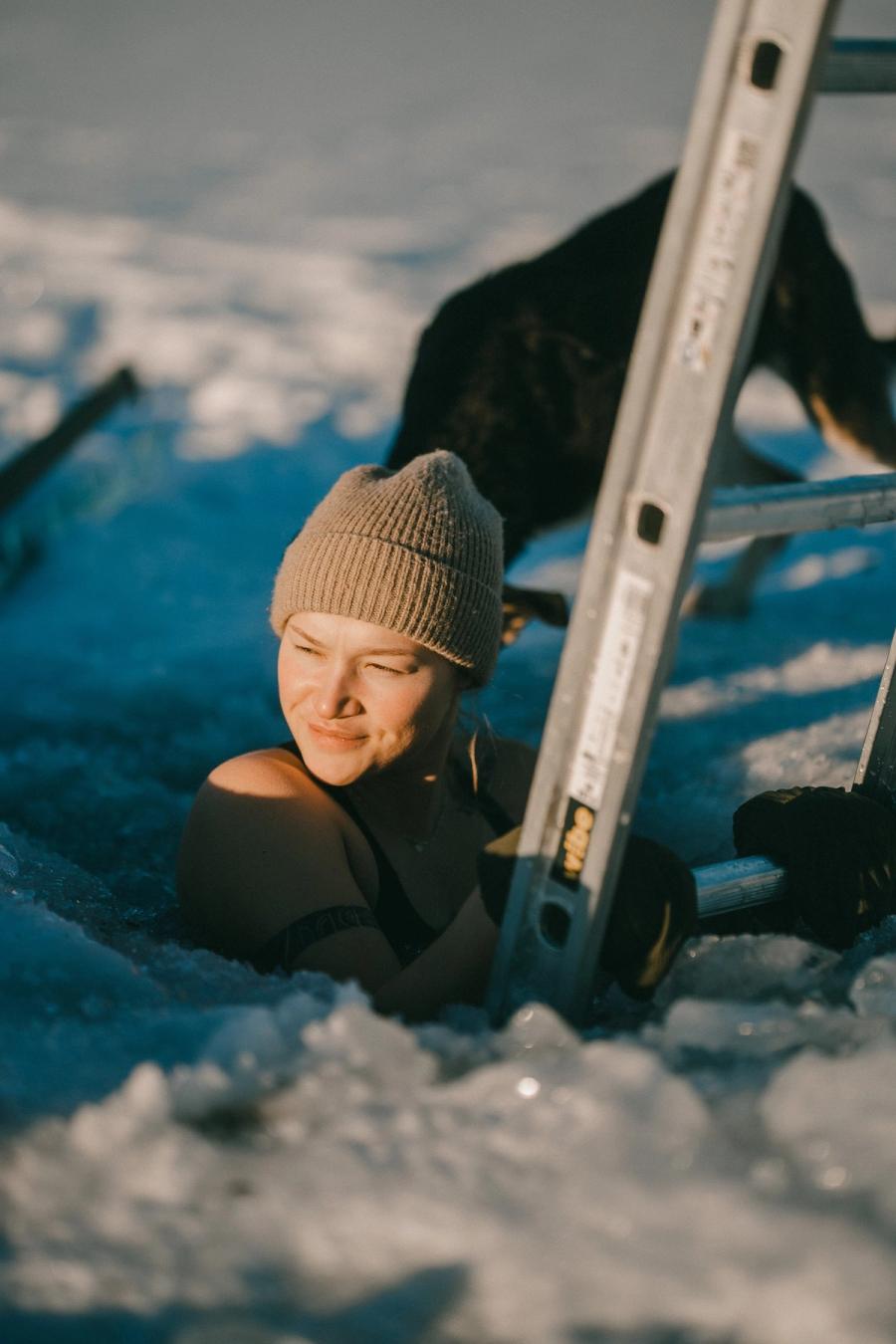 En gjest med ullue i isråket, med hendene på stigen, mens en hund venter på snøen