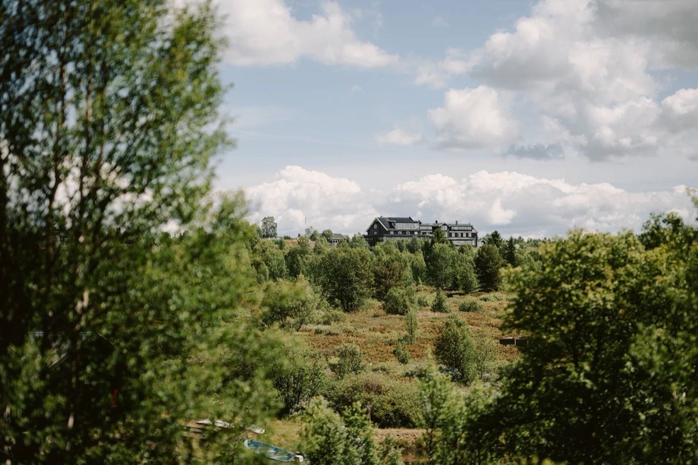 Nøsen Fjellhotell sett over grønn skog og lyngmark en sommerdag