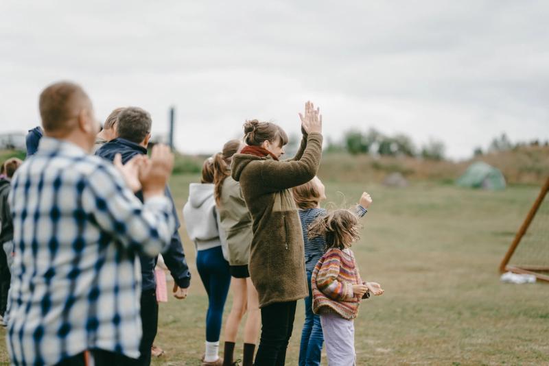 Adults and children clapping together outdoors