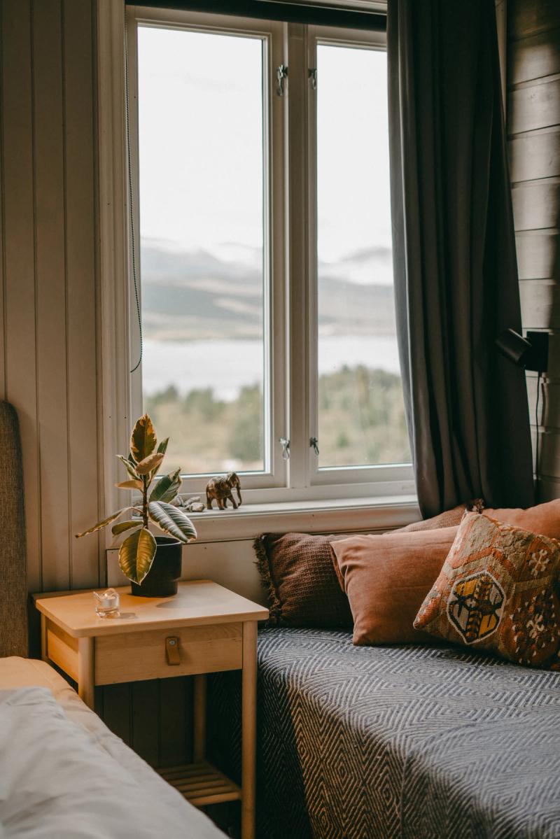 A bed by the window, with the lake and hills beyond