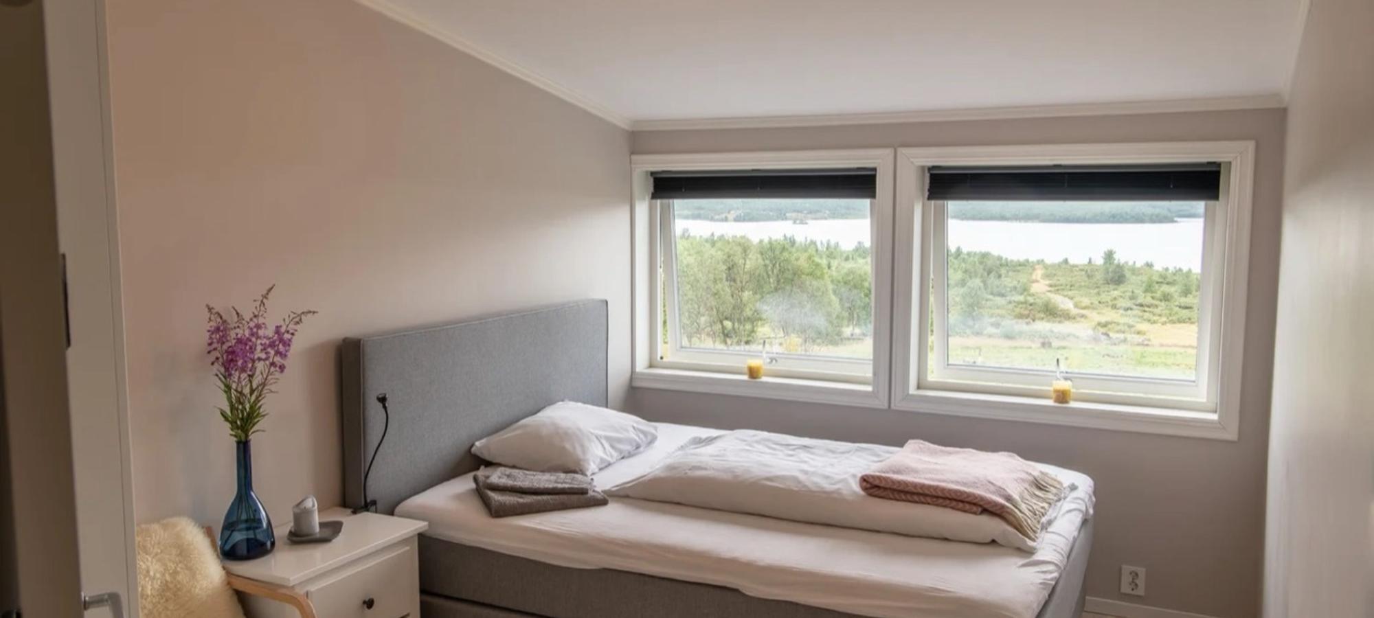 Et lyst hotellrom med dobbeltseng og vinduer mot fjellene