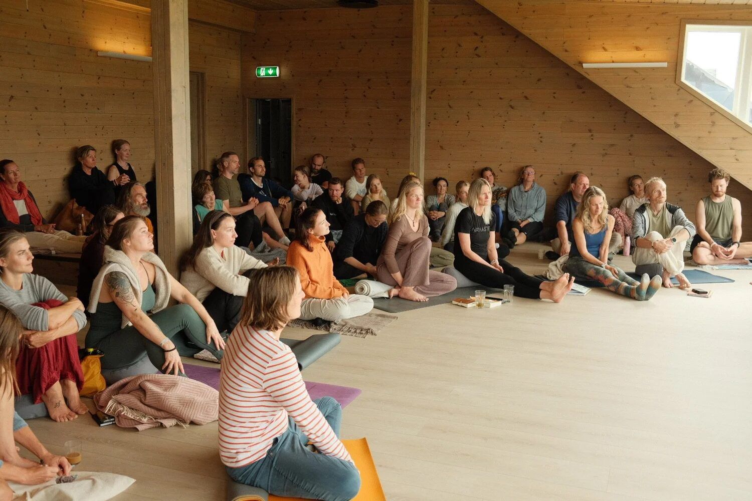 Students sitting on their mats in a bright shala, listening to a talk