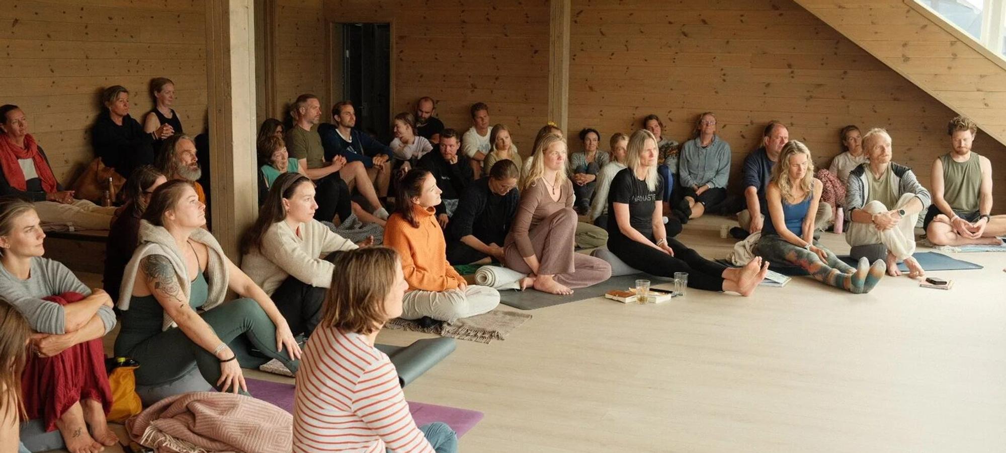 Students sitting on their mats in a bright shala, listening to a talk