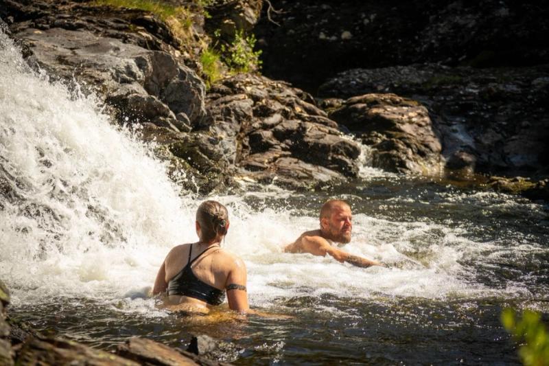Two people bathing below a waterfall