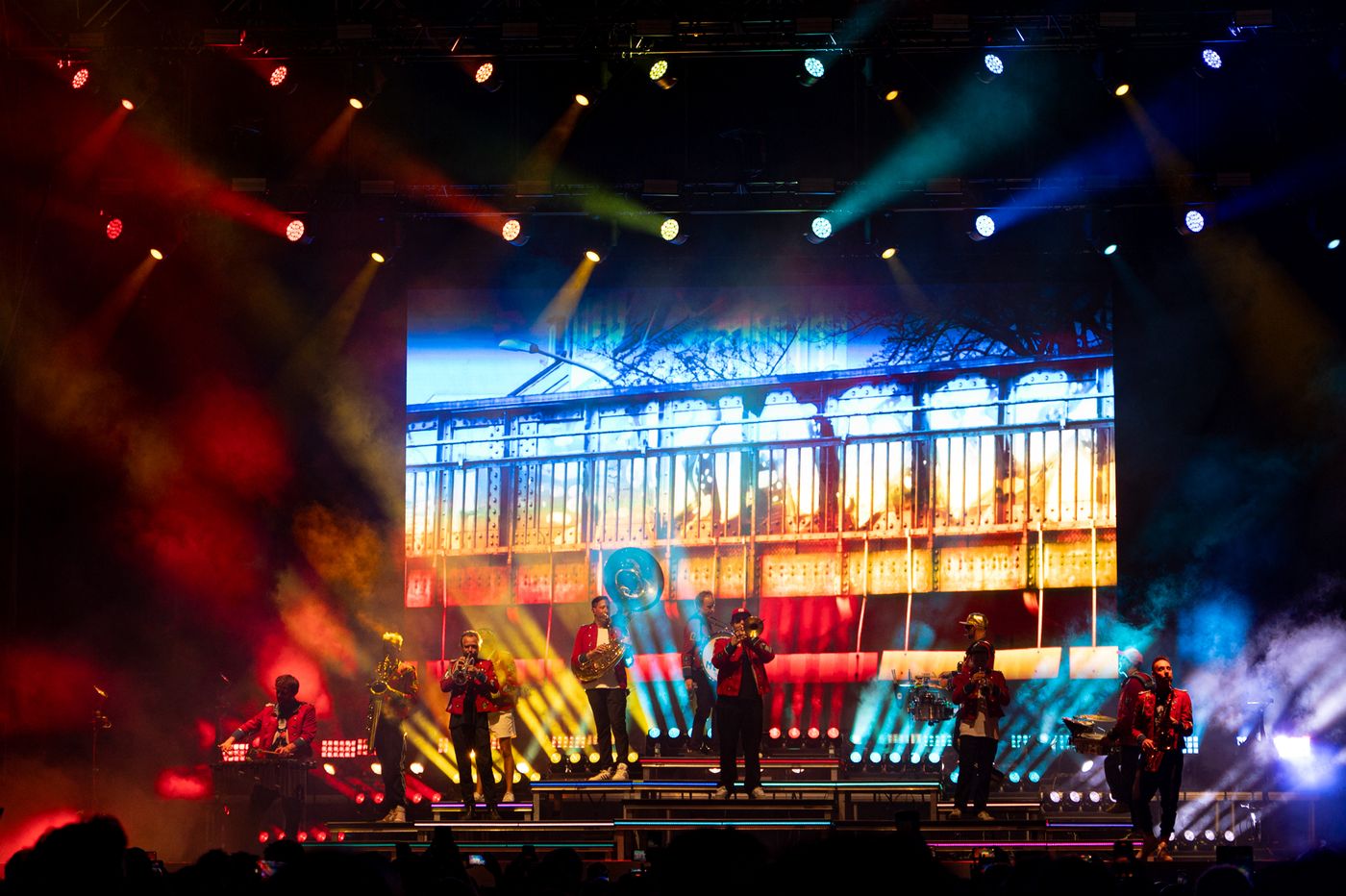 Toda la banda de Meute tocando sobre el escenario con visuales de colores proyectados