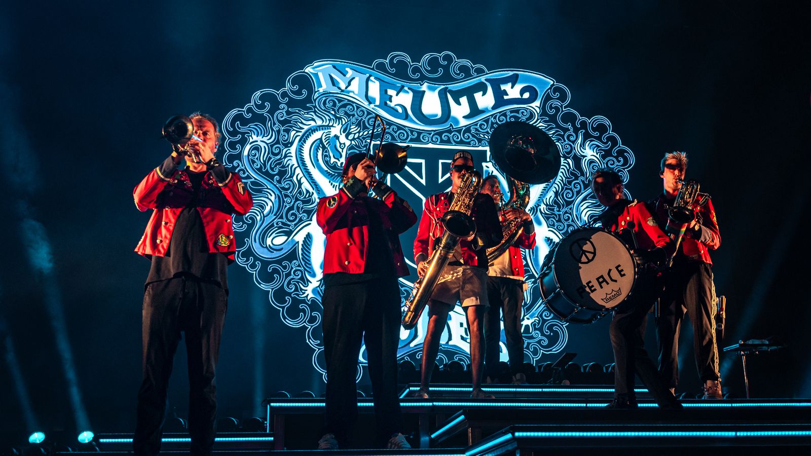 Los músicos de Meute tocando en vivo sobre el escenario, con el logo de la banda proyectado detrás