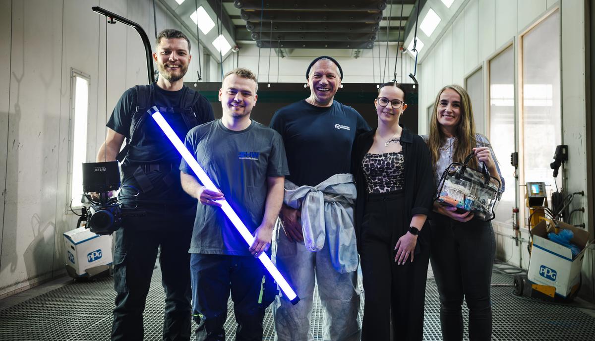 Fünfköpfiges Filmteam in einer industriellen Werkhalle mit Kamera-Equipment und leuchtender blauer LED-Lichtröhre.
