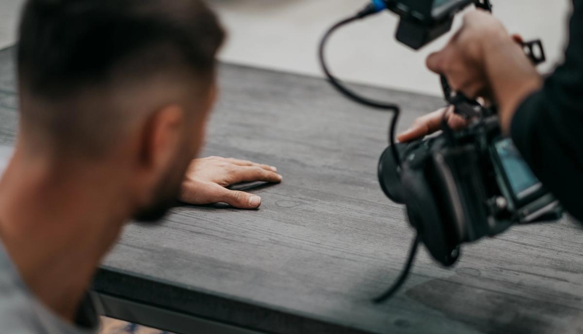 Nahaufnahme: Die Kamera filmt dicht über der Tischplatte die aufgelegte Hand eines Handwerkers.