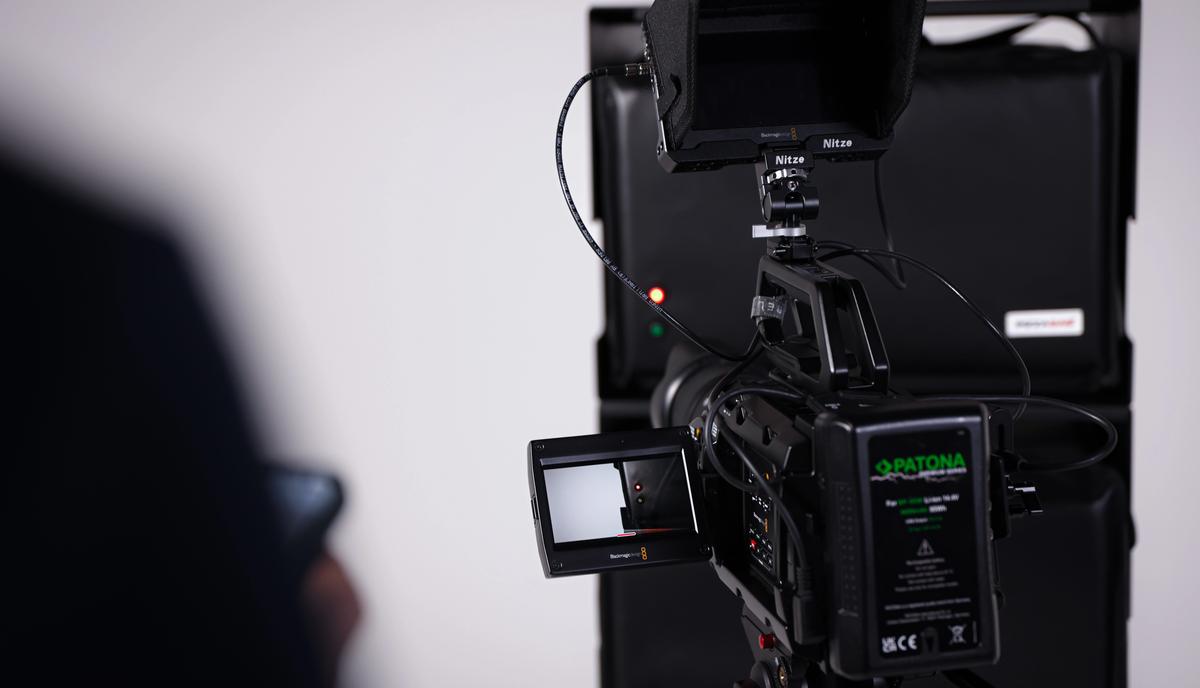 Nahaufnahme der Filmkamera mit eingeschaltetem Monitor, dahinter der weiße Studiohintergrund.