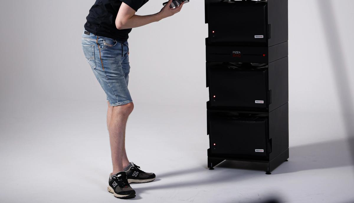 Ein Mann richtet im Studio einen Stapel schwarzer Boxen aus, vorn unscharf die Kamera.