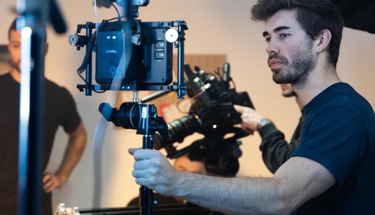 Ein Kameramann steht hinter einer Filmkamera auf dem Stativ, darüber eine große Softbox.