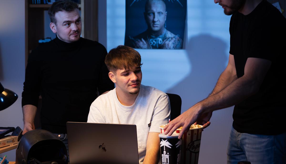 Drei Crewmitglieder arbeiten im abgedunkelten Raum an einem Tisch mit Laptops und Kameratechnik.