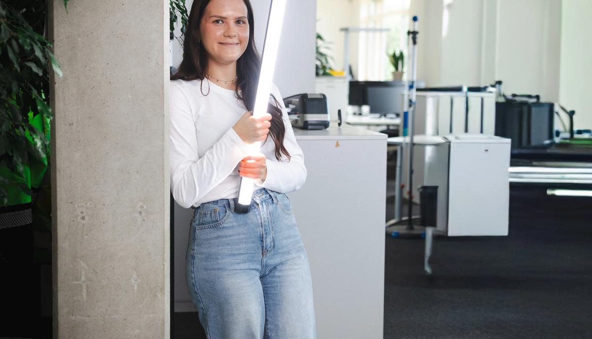 Frau in einem modernen Büro mit leuchtender LED-Lichtröhre neben einer Betonsäule.