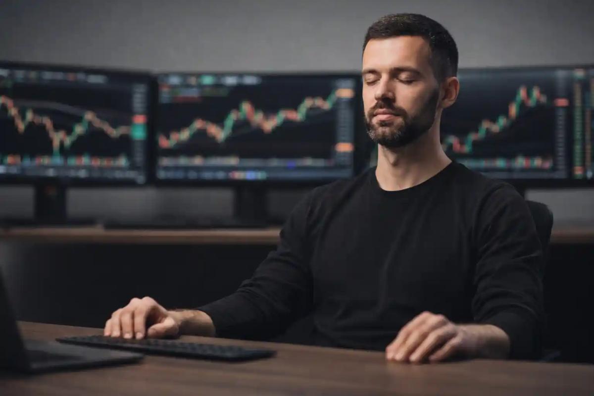 Trader meditating at a multi-monitor trading desk with blurred charts in the background