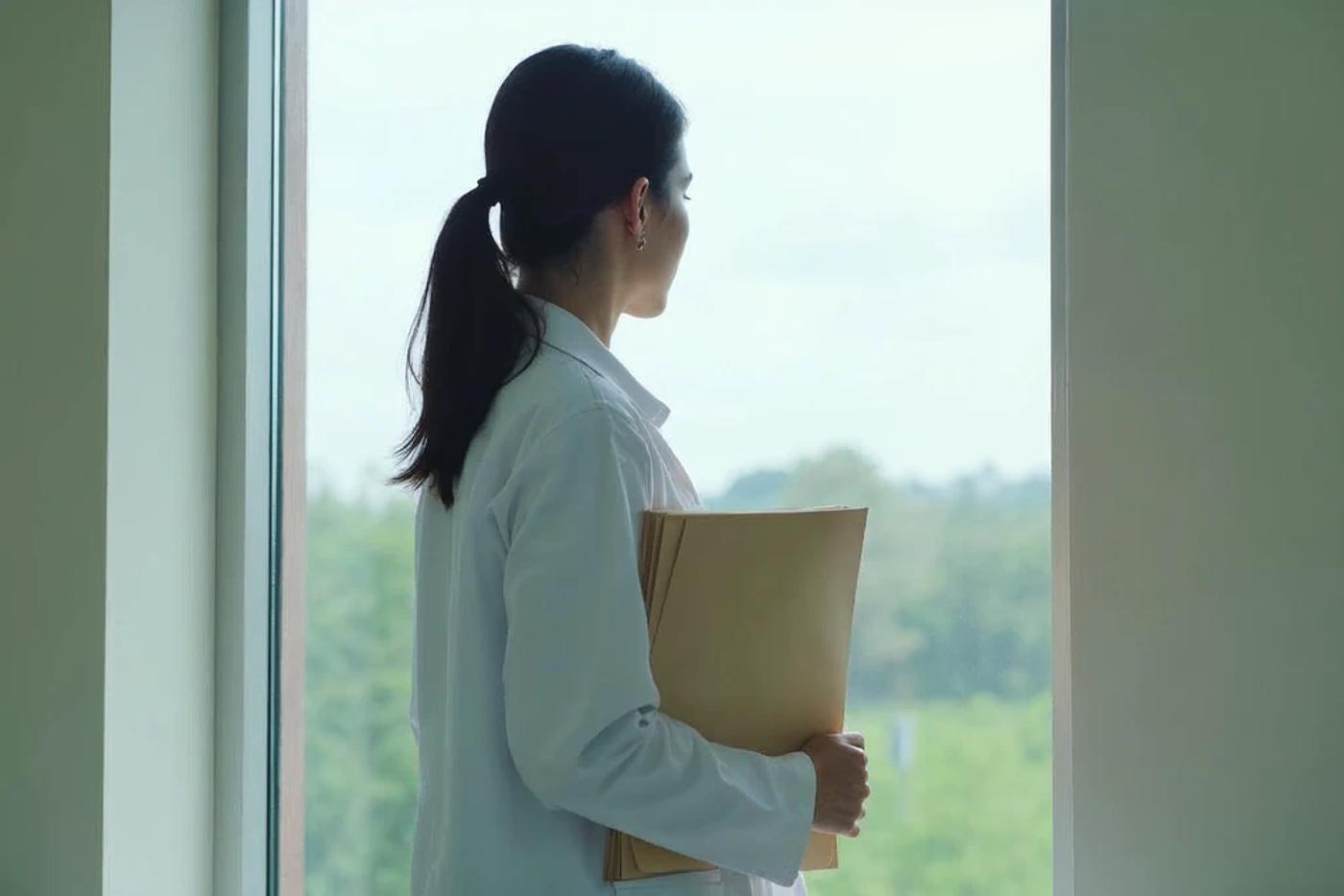Physician holding a folder by a window, weighing Stark Law vs Anti-Kickback Statute questions before investing