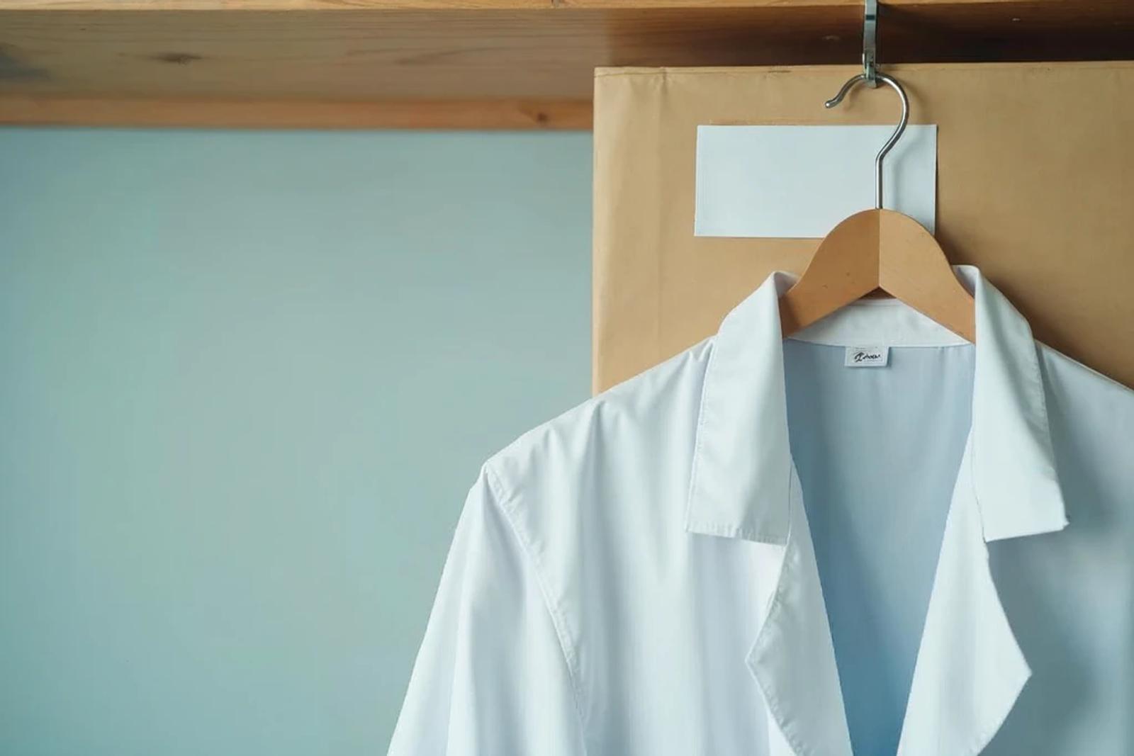 A physician's white coat hanging on a hook beside a closed insurance folder