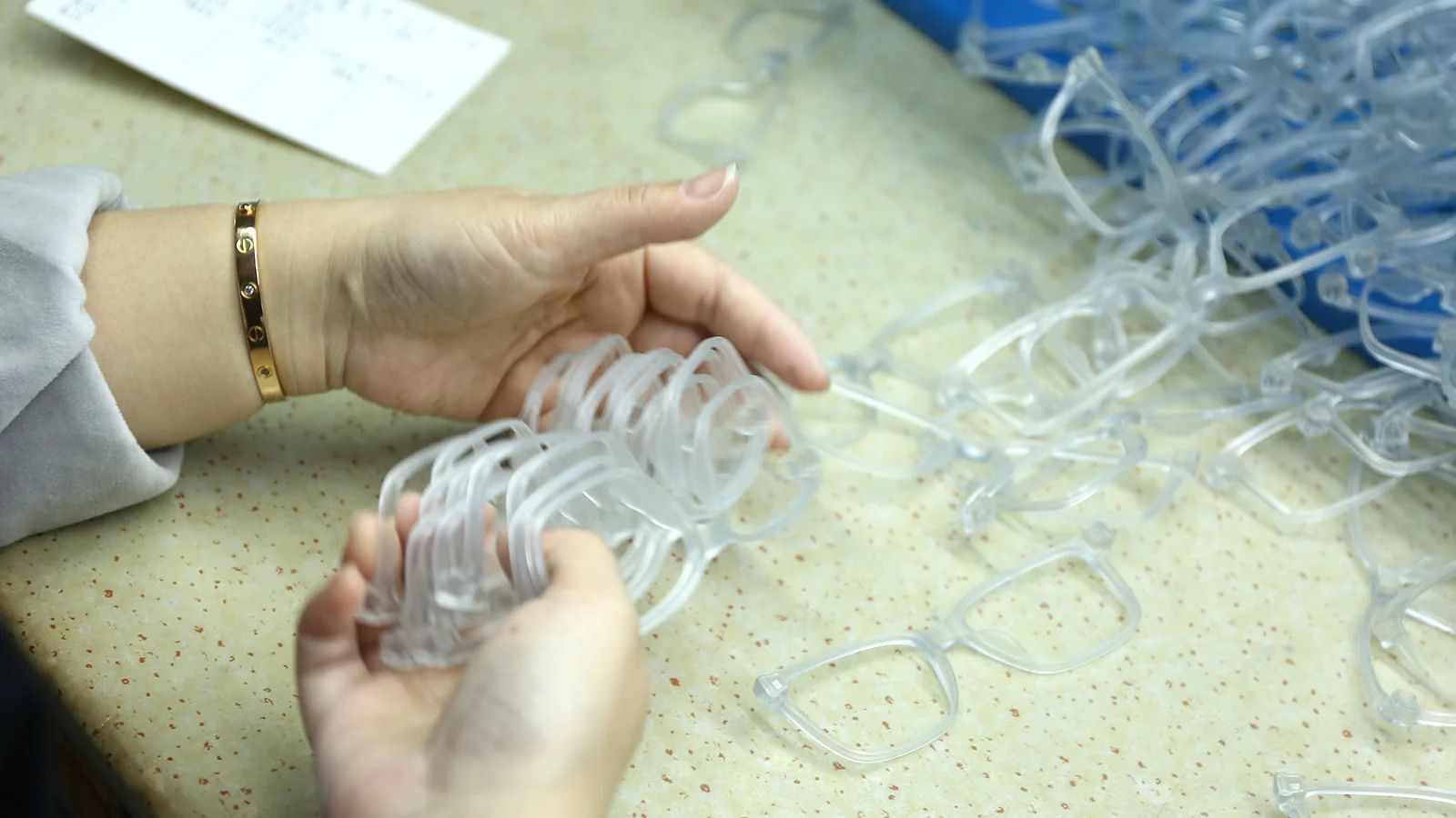 DOMI worker handling clear sunglasses frames during production preparation