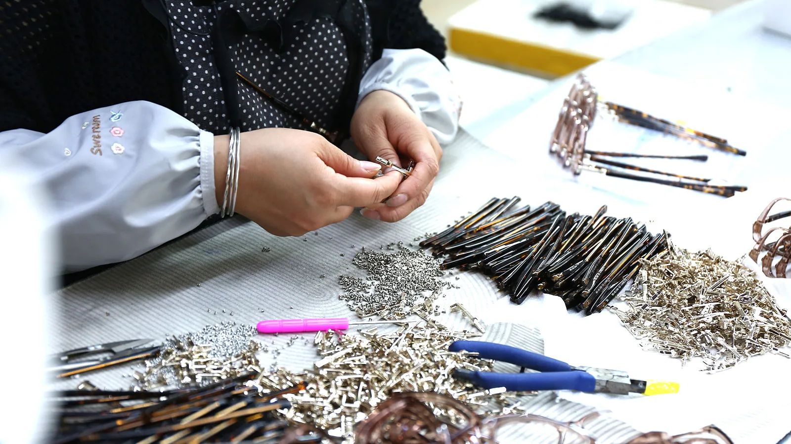 Worker installing metal hinges into sunglasses temples during assembly