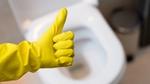 Hand in yellow rubber glove showing-thumb-up-sign above a white toilet bowl