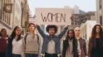 Seven women in a line one holding a sign saying "women"