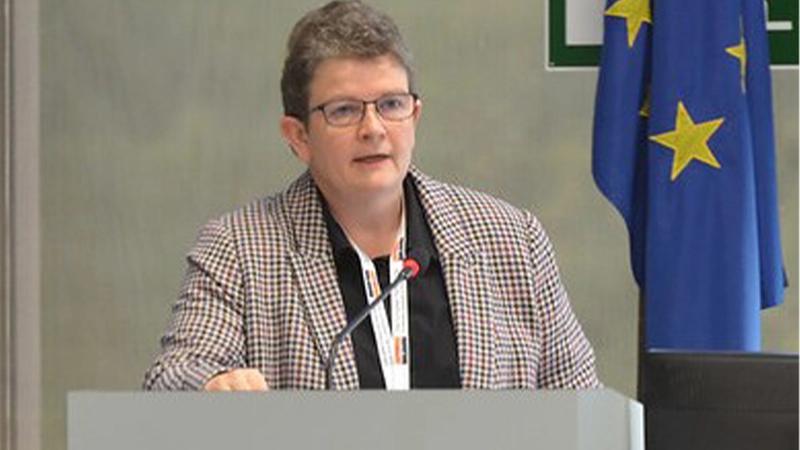Julia Fentem speaking at a rostrum with EU flag to the right