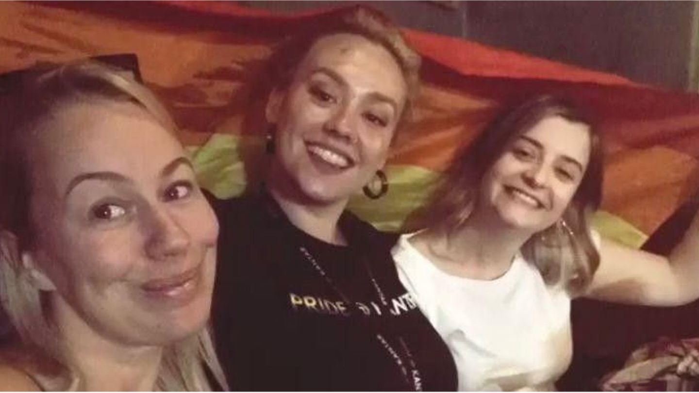 Picture of Angharad and two friends holding a rainbow flag