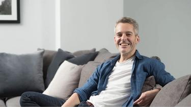 Image for Dove Men+care with a man sited on a grey couch and smiling to the camera"