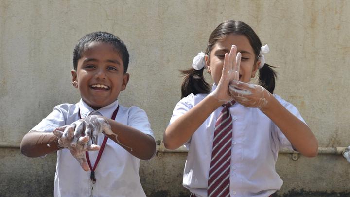 Two school children looking at camera showing them washing hands